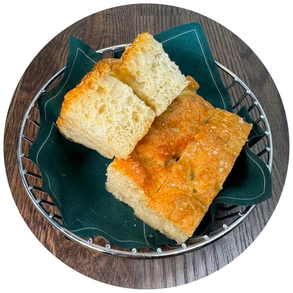Golden-brown crusty bread pieces arranged in a metal basket lined with a dark green cloth on a wooden table.
